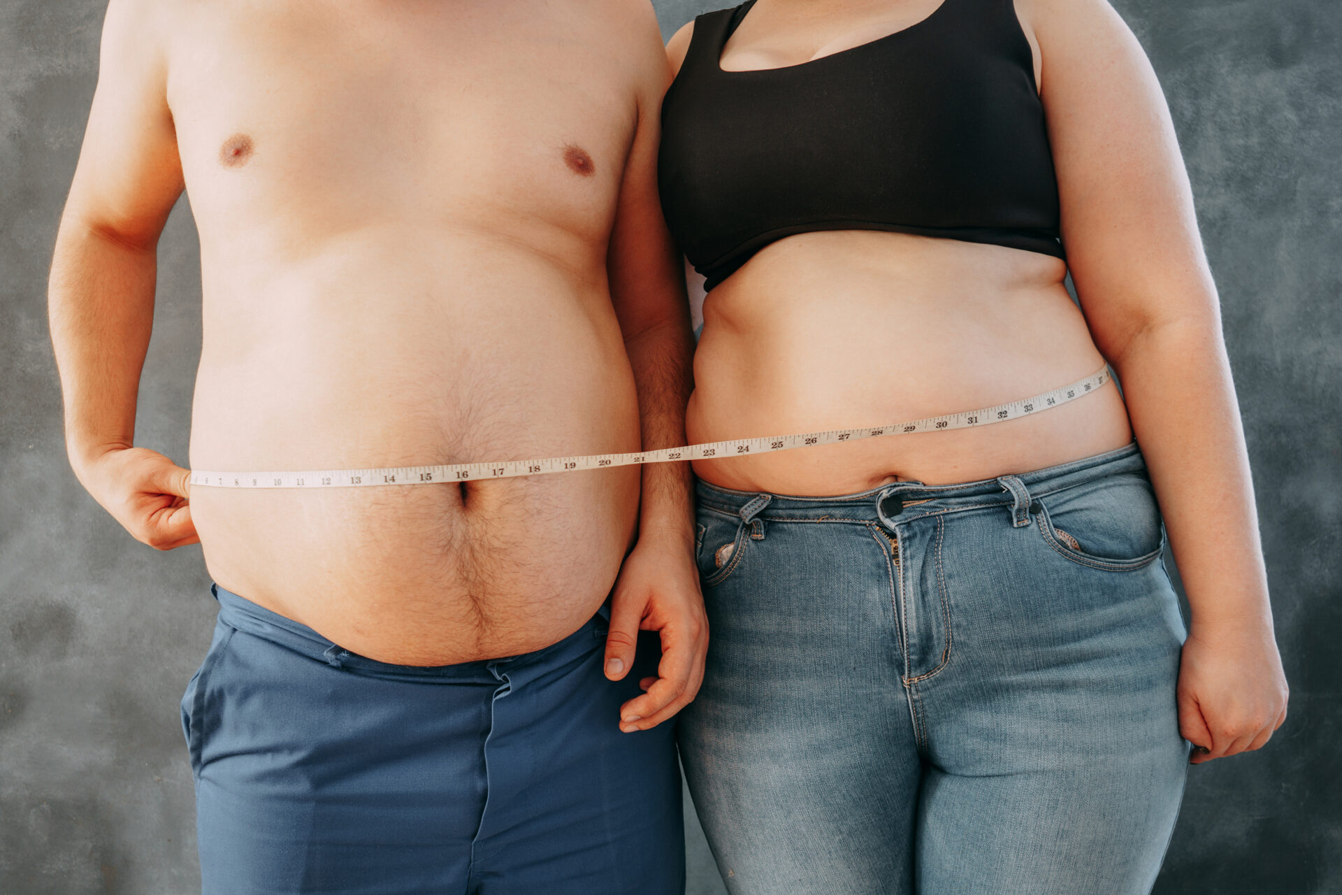 overweight couple standing together wrapped with measure tape. d